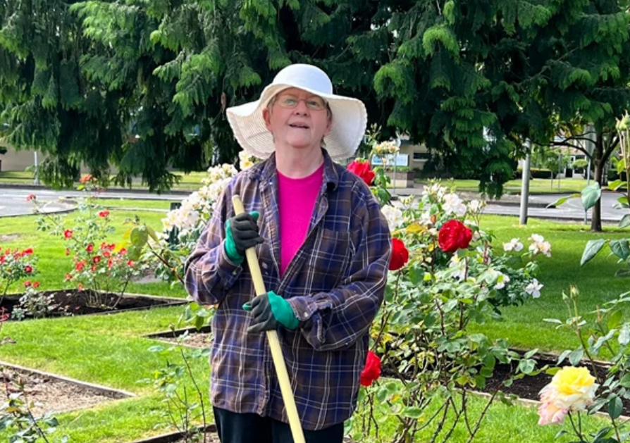 Master Gardener smiling, with floppy hat and red roses in the background.